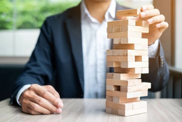 businessman in suit pulling jenga blocks from a tower on a table